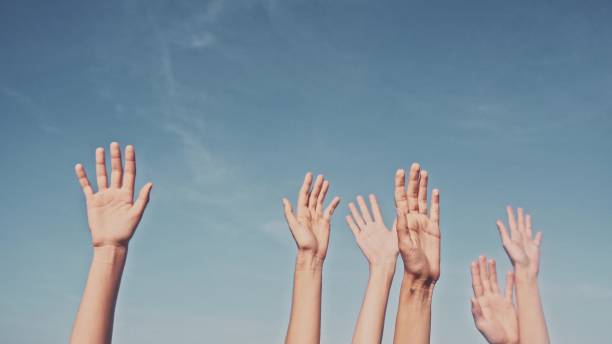 istock People rasing hands on blue sky background. Voting, democracy or volunteering concept 970504334