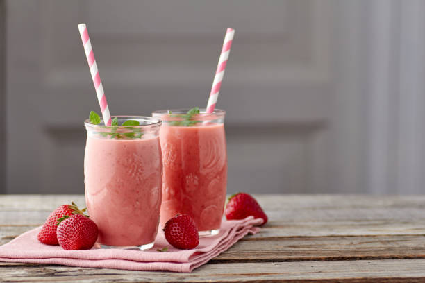 Yogurt and strawberry smoothie in two jars with drinking straw on wooden table stock photo