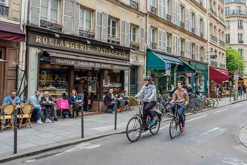 Paris / France - May 13, 2018: People ride bikes through the charming, beautiful, old Marais neighborhood, known for its shopping and dining and many historical sites.