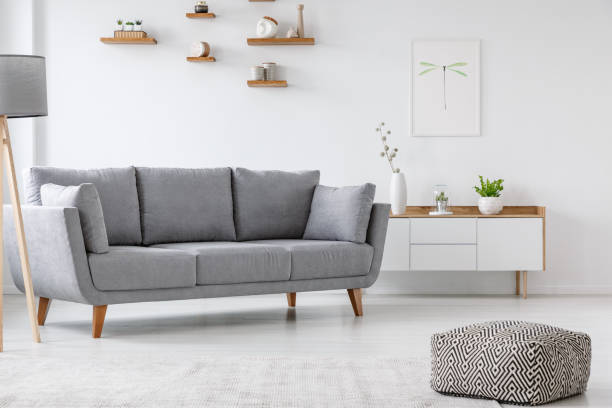 istock Patterned pouf and grey couch in minimal living room interior with poster above cupboard. Real photo 970545252