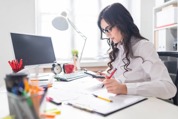 una joven está sentado en el escritorio de la oficina, trabajando con una calculadora y documentos. - economist fotografías e imágenes de stock