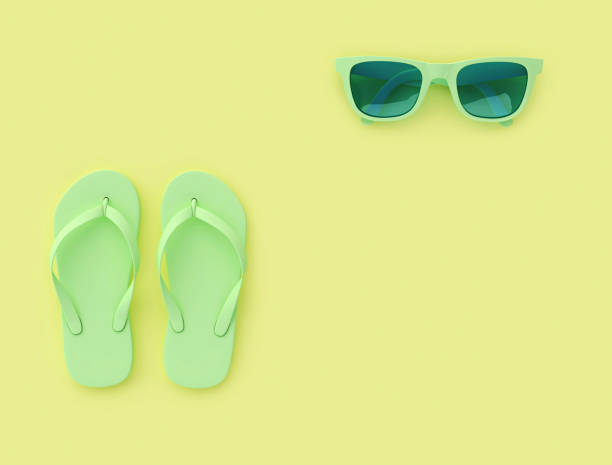 Light green flip flops and sunglasses on yellow background with copy space