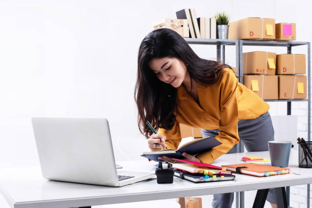 istock The lady is working e-commerce,checking order from laptop and write on book,plenty of post box prepare for shipping on shelf. 970679110