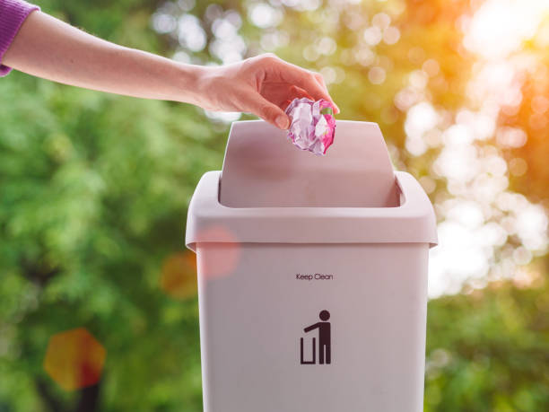 istock female hand trowing a paper into a garbage bin on bokeh background. cleaning concept. 970714844