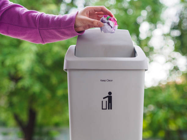 istock female hand trowing a paper into a garbage bin on bokeh background. cleaning concept. 970714916