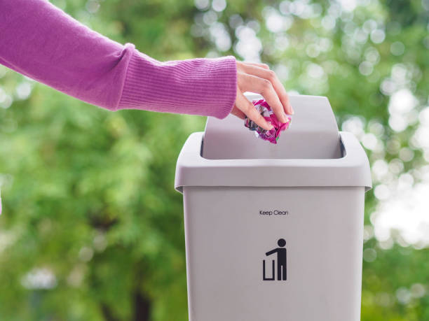 istock female hand trowing a paper into a garbage bin on bokeh background. cleaning concept. 970715294
