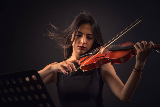bastante joven mujer tocando un violín sobre fondo negro - violin women violinist music fotografías e imágenes de stock
