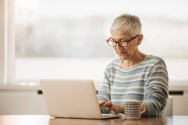 istock Smiling mature woman typing an e-mail on laptop while sitting at the table at home. 970729666
