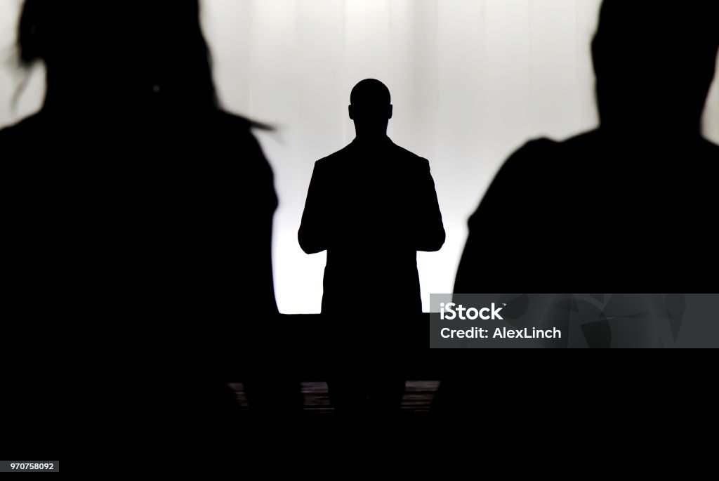 Silhouettes of a mystery man standing , watching and confronting two blurry persons Silhouettes of a mystery man standing , watching and confronting two blurry persons in the dark Preacher Stock Photo