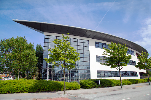 Swansea, UK: May 21, 2018: Modern glass and steel office building exterior with an architectural feature roof - in a business park with landscaping and a blue sky background.