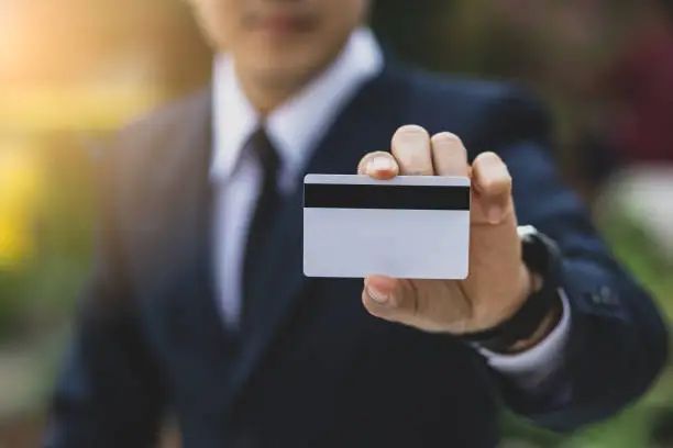 Young businessman hand holding blank white credit card mock up front side view, Empty plastic bank-card design mock up, money and finances concept