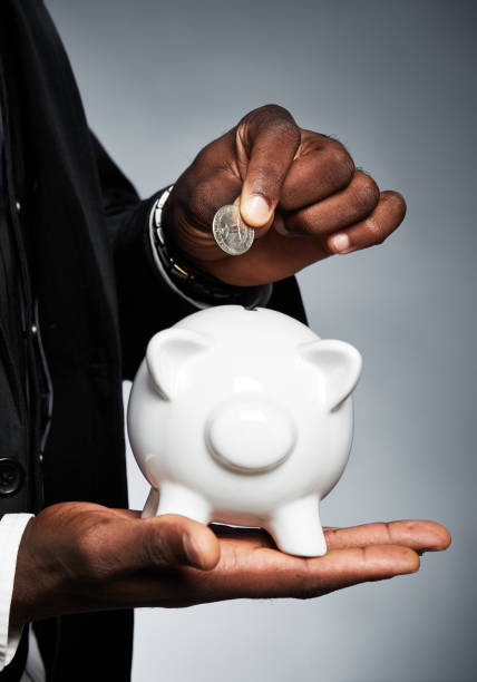 A man's hands hold a white ceramic piggybank about to add a coin.