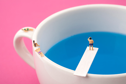 miniature people in mug cup swimming pool.