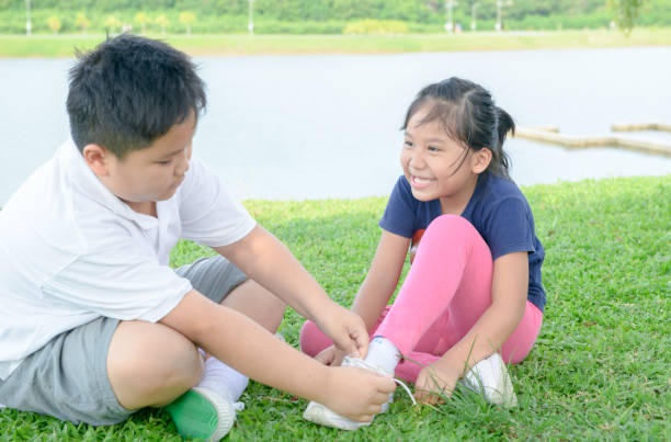 Happy sister smiles to her brother Asian sister smiles to her brother while he is helping to tie her shoes in Health park. love and care concept child tied up stock pictures, royalty-free photos & images