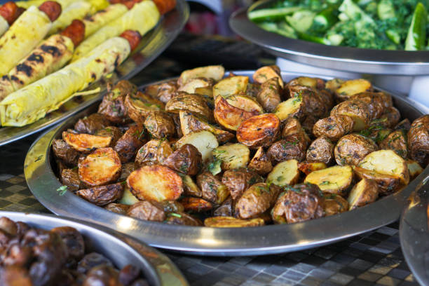 Dinner table with meat grill, roast new potatoes, vegetables, salads, sauces, snacks and lemonade Grilled sausage, mushrooms. Stock Photo