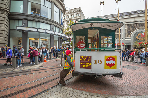 San Francisco, CA, USA - August 15, 2016: Cable car operators push the turntable around the reverse direction in Powell and Market St Turntable or terminus while crowds of tourists waiting to go up.