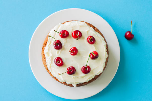 crème sure maison gâteau avec glaçage au fromage à la crème orné de cerises mûres fraîches sur un fond bleu clair. vue de dessus. - baked cheese topping photos et images de collection