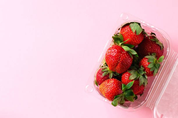 istock Plastic container with fresh ripe strawberries on a light pink background. Top view and copy space. Organic food concept. 970806712