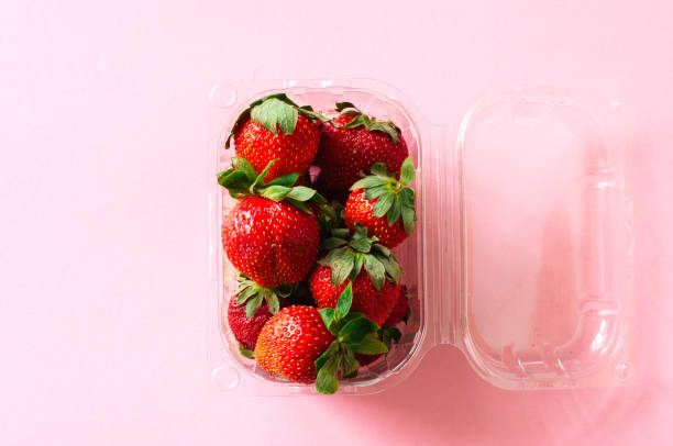 istock Plastic container with fresh ripe strawberries on a light pink background. Top view and copy space. Organic food concept. 970806716