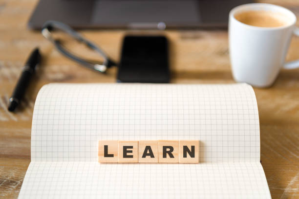 istock Closeup on notebook over wood table background, focus on wooden blocks with letters making Learn text 970816340