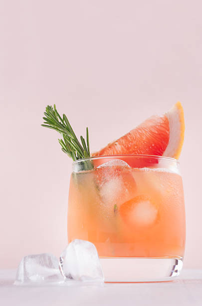istock Cold grapefruit cocktail decorated twig rosemary and slice citrus closeup on pink background, vertical. 970819382