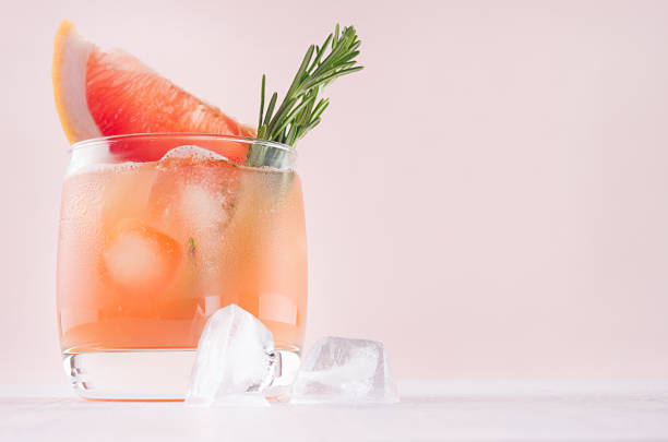 istock Summer fresh homemade grapefruit lemonade with ice cubes and rosemary on light pink background. 970819454