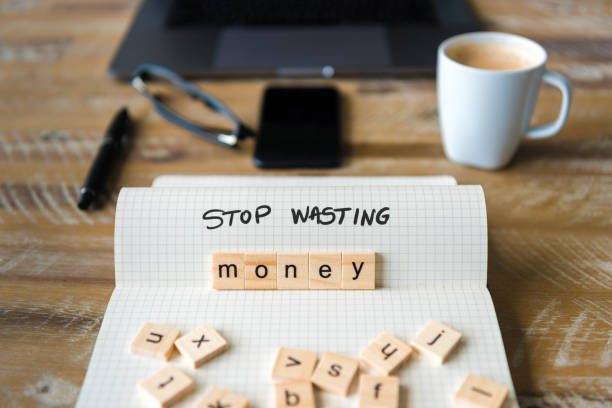 istock Closeup on notebook over wood table background, focus on wooden blocks with letters making Stop Wasting Money text 970819946