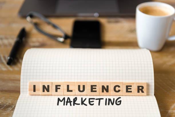 istock Closeup on notebook over wood table background, focus on wooden blocks with letters making Influencer Marketing text 970820180