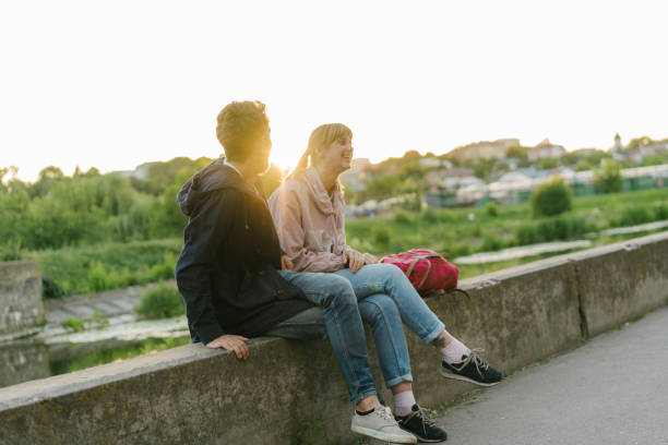 istock Man and woman sitting near the river at sunset 970829068