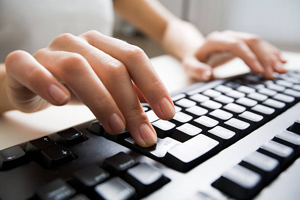 Typing Close-up of female hands typing on computer keyboard; businesswoman pressing enter key with her middle finger while working at office desk. enter key stock pictures, royalty-free photos & images