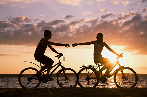 Silhouettes of happy couple riding their bicycles on seashore at sunset