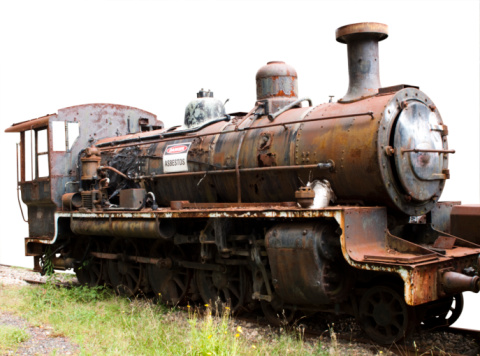 Old rusty steam locomotive with sign 'Danger asbestos' standing on the gras, isolated on white background with copy space