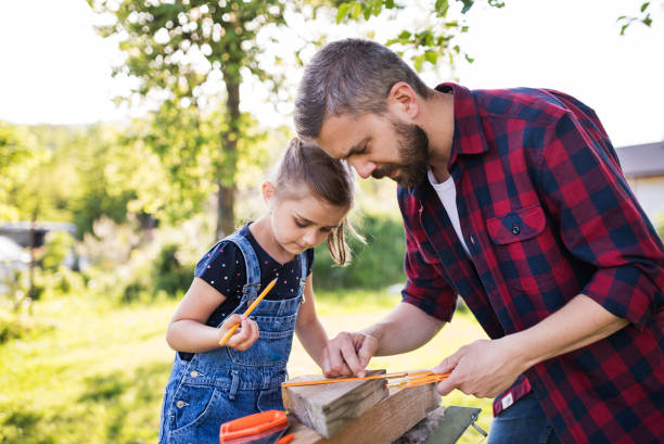 Father with a small daughter outside, making wooden birdhouse. Handsome father with a small daughter outside, making wooden birdhouse or bird feeder. Birdhouse stock pictures, royalty-free photos & images