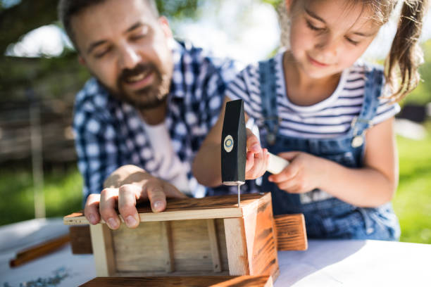 Father with a small daughter outside, making wooden birdhouse. Father with a small daughter outside with hammer making wooden birdhouse or bird feeder. girl with a hammer stock pictures, royalty-free photos & images