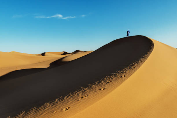 Traditional dressed Moroccan man with turban stands on a sand dune in the Sahara desert. stock photo