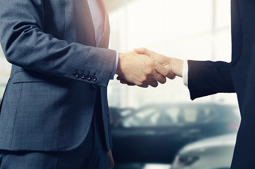 salesman and customer handshake after successful deal in car dealership