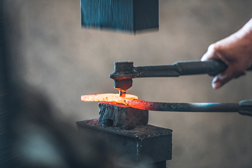Close-up shot of blacksmith shaping peace of metal with hydraulic press machine in his workshop in Malaysia.