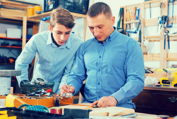 istock father and teen son working with wood plank in workshop 970868596