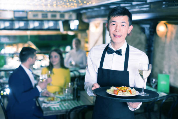 istock Man waiter is holding tray with wine and salad for clients 970872426