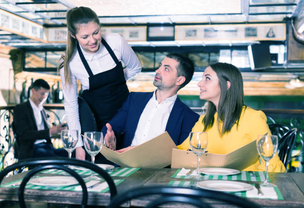 istock Female waiter is taking order from smiling couple with menu who is dinning 970872448