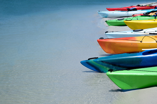 eight canoes all bright different colors on the edge of a tropical sandy beach the canoes are in a line on the right on the left is a calm clear blue sea ideal for text space horizontal format