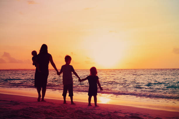 istock mother with kids walking on beach at sunset 970899518