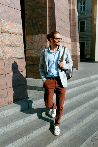 Men Style. Handsome Smiling Man On Street. Fashionable Male Wearing Glasses And Business Casual Men's Attire With Backpack Walking On Sunny City Street. Office And Work Fashion Clothes. High Quality