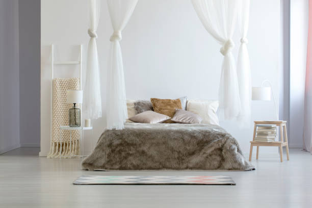 istock Lamp on table next to bed with pillows under canopy in bright scandi bedroom interior. Real photo 970923862