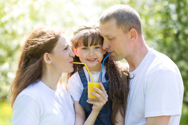 istock Dad, mom and daughter drink juice from one glass. 970923992
