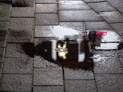 A pedestrian walk symbol reflecting in a puddle during night in a bright city environment