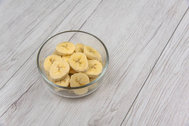 istock Raw yellow banana fruit slices in a bowl on white wood table 970975252
