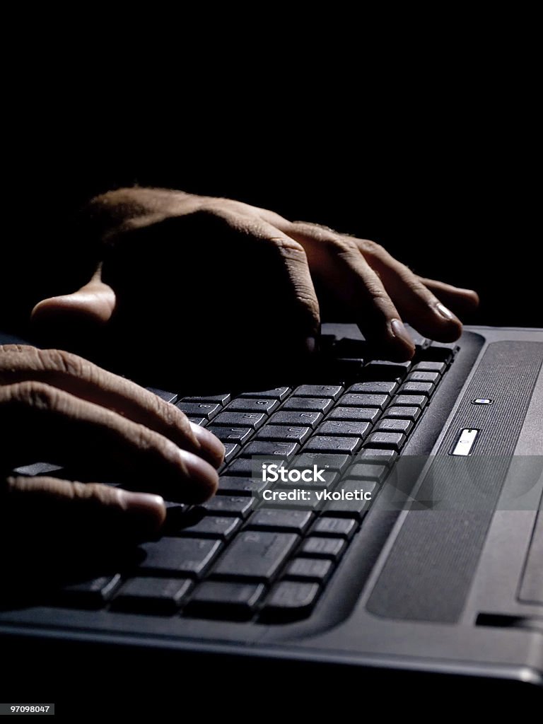 Hands on a black laptop keyboard in the dark male hands on the keyboard,low key and high contrast,may suggest cyber crime, hacking,spying Criminal Stock Photo