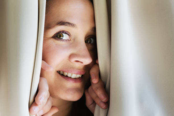istock Beautiful young woman peeks through drapes 970995766
