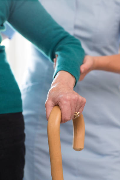 istock Senior Womans Hands On Walking Stick With Care Worker In Background 971008062